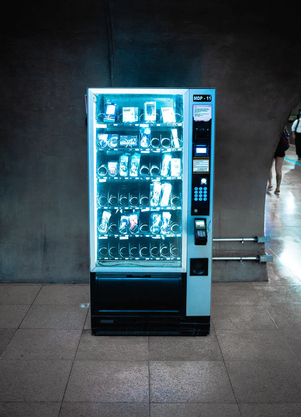 An illuminated snack vending machine with a selection keypad and payment terminal.